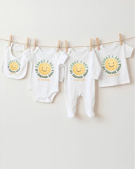 A row of four white baby clothes with a cheerful smiley face design, hanging on a clothesline.