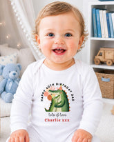 A smiling baby wearing a white onesie with a cartoon alligator and text that says "Happy 40th Birthday Dad lots of love Charlie xxx".