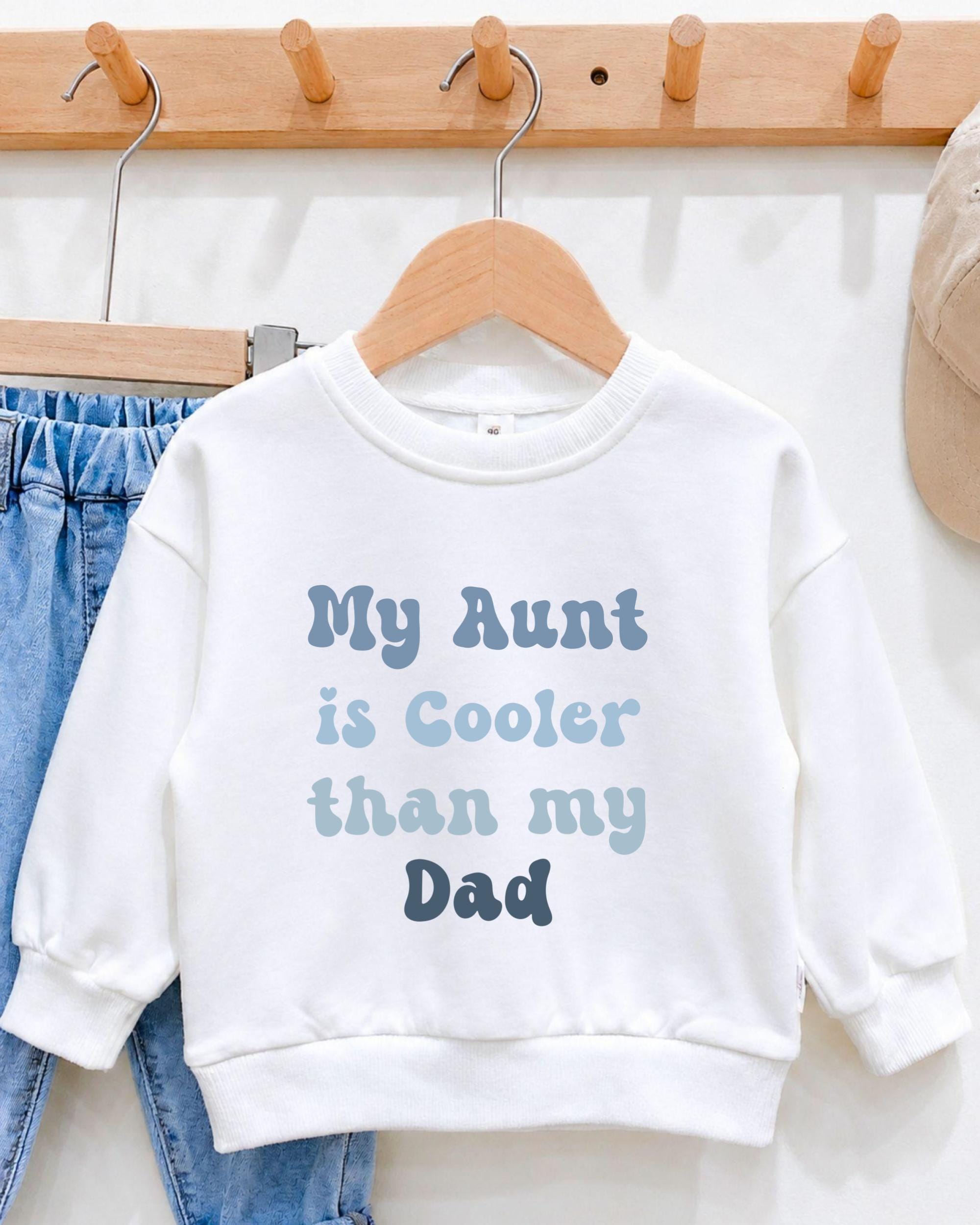 A white sweatshirt with text printed on it, hanging on a wooden hanger.