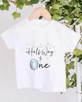 A white t-shirt with a graphic design and text printed on it, hanging on a wooden hanger.
