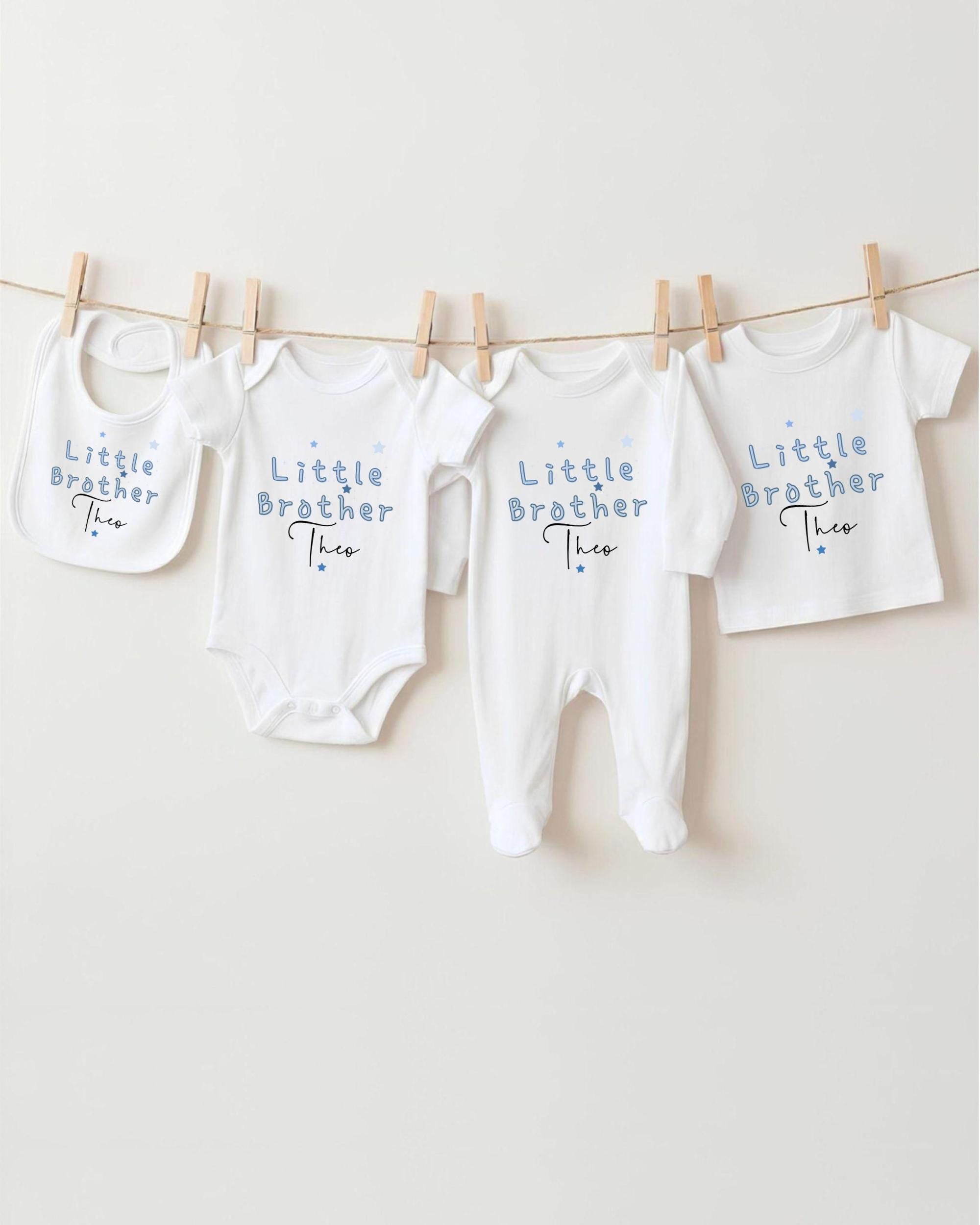 A row of four white baby clothes with the text "Little Brother Theo" printed on them, hanging on a clothesline.