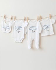 A row of four white baby clothes with the text "Little Brother Theo" printed on them, hanging on a clothesline.