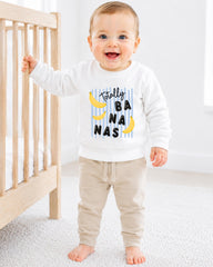 A smiling baby boy wearing a white sweatshirt with a banana graphic and the text "Totally BANANA NANA" printed on it.