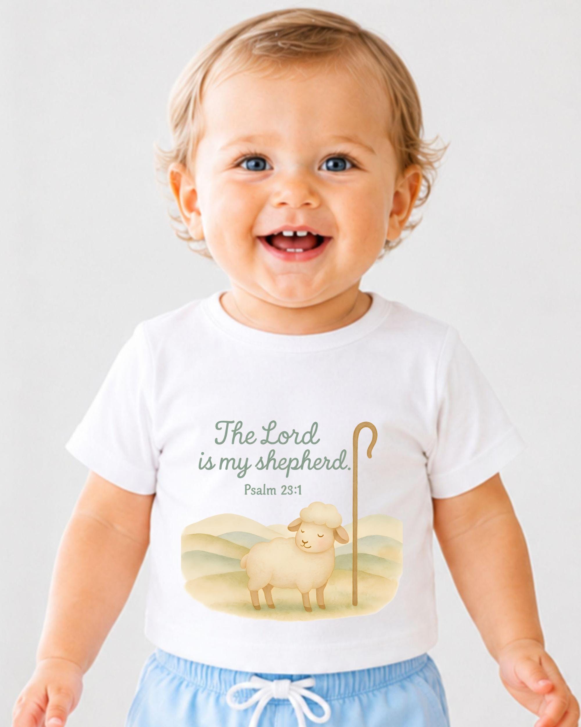 A smiling baby boy wearing a white t-shirt with a Bible verse and an illustration of a sheep.