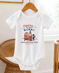 A white baby onesie with a graphic design on it, hanging on a wooden hanger.