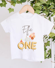 A white t-shirt with a personalized text and graphic design, hanging on a wooden hanger.