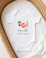 A white baby onesie with a graphic of a carrot, radish, and tomato, along with the text "Bappy Miller Locally grown".