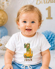A smiling baby boy wearing a white t-shirt with a cartoon image of a car and the name " Josh" printed on it.
