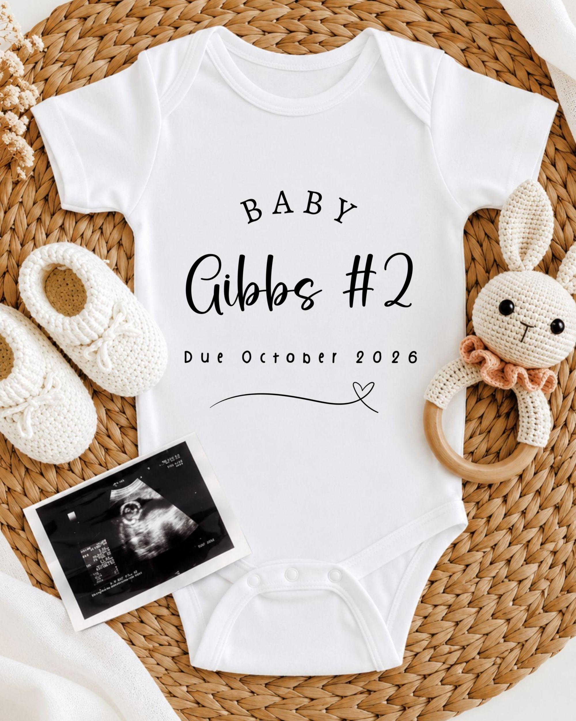 a baby announcement, including a white onesie with the text "BABY Gibbs #2 Due October 2026", a crocheted bunny toy, and a black and white photograph of an Ultrasound image.