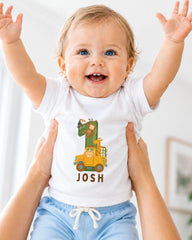 A smiling baby wearing a white t-shirt with a cartoon character and the name " Josh" printed on it, being held up by someone's arms.