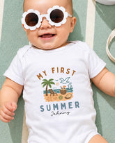A baby wearing a white onesie with a graphic design and text, lying on a green and white striped surface.