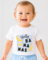 A smiling baby wearing a white t-shirt with a graphic design of bananas and the text "Totally Banana" printed on it.