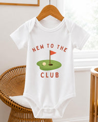 A white baby onesie with the text "NEW TO THE CLUB" printed on it, along with a golf hole and flag graphic.