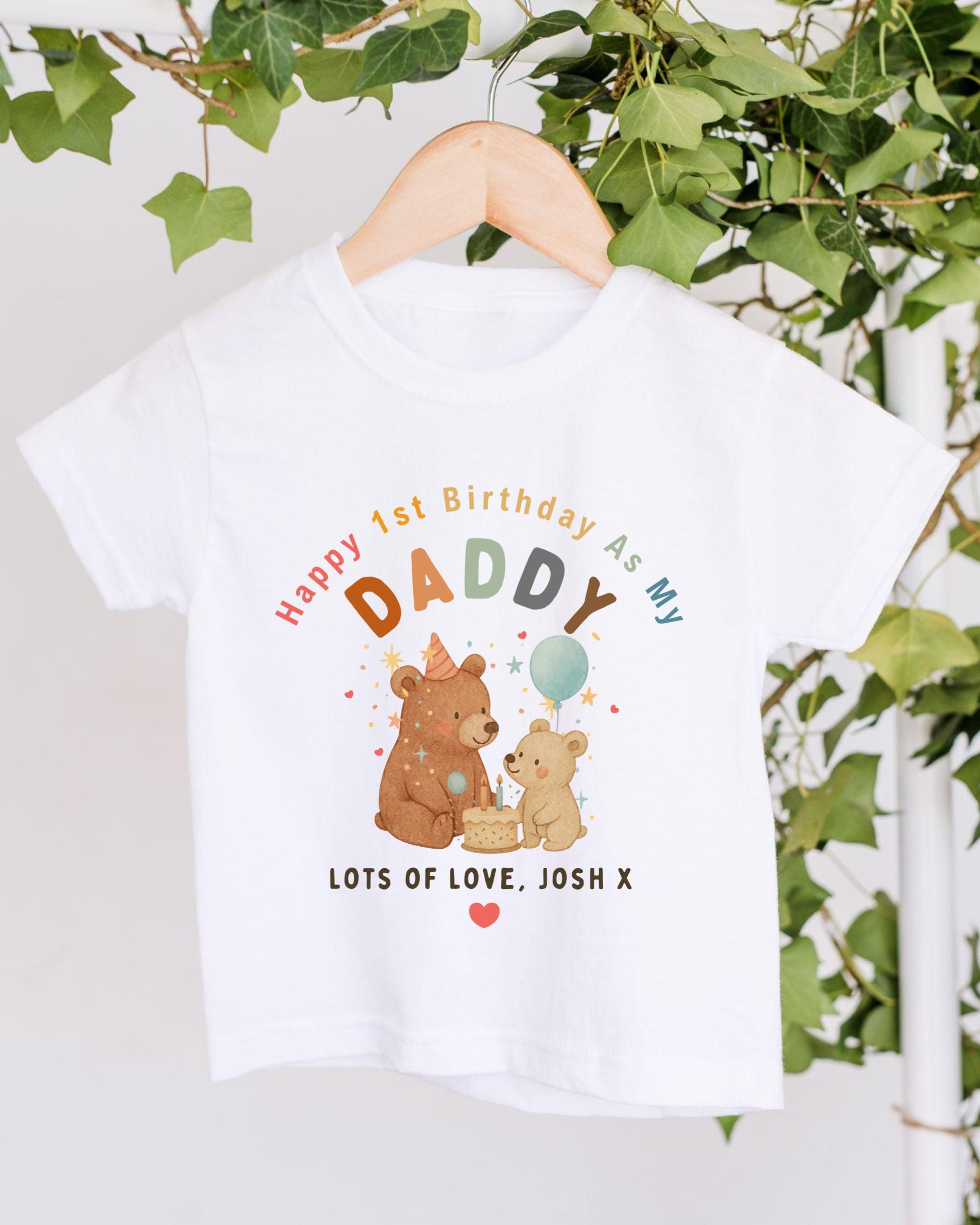 A white t-shirt with a colorful graphic design featuring two bears and a balloon, along with text that reads "Happy 1st Birthday As My Daddy Lots of Love, Josh X".
