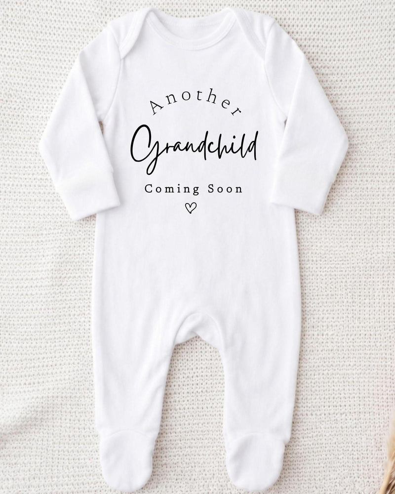 A white bodysuit with the text "Another Grandchild Coming Soon" printed on it.