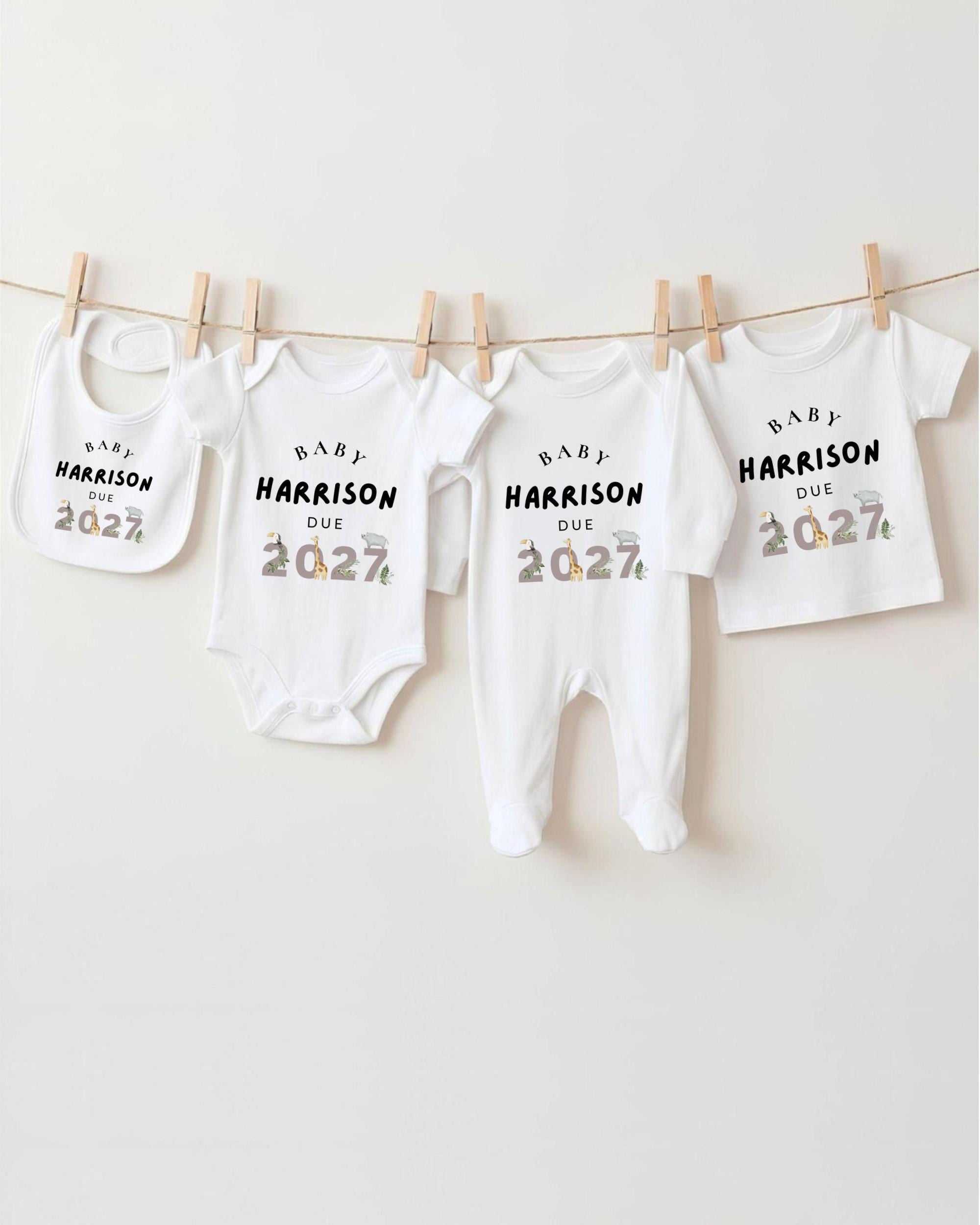 A row of white baby clothes with the text "BABY HARRISON DUE 2027" printed on them, hanging on a clothesline.