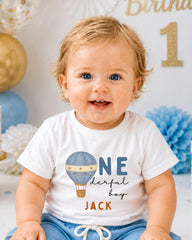 A smiling baby boy wearing a white t-shirt with a hot air balloon design and the text "ONE derful BOY JACK" printed on it.