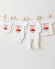 A collection of white baby clothes, including onesies and bibs, with red illustrations of fire trucks and the text "Halfway to One" printed on them.