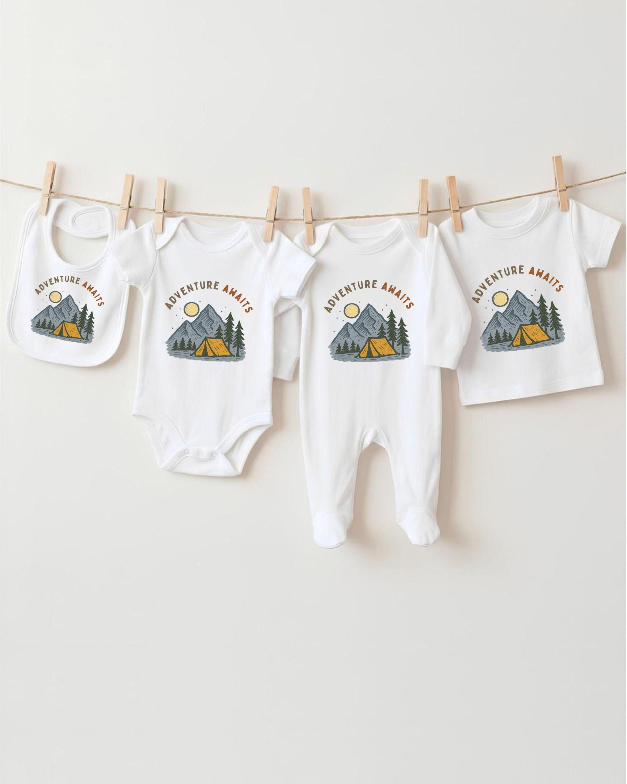 A collection of baby clothes, including onesies and a bib, hanging on a clothesline with camping-themed designs.