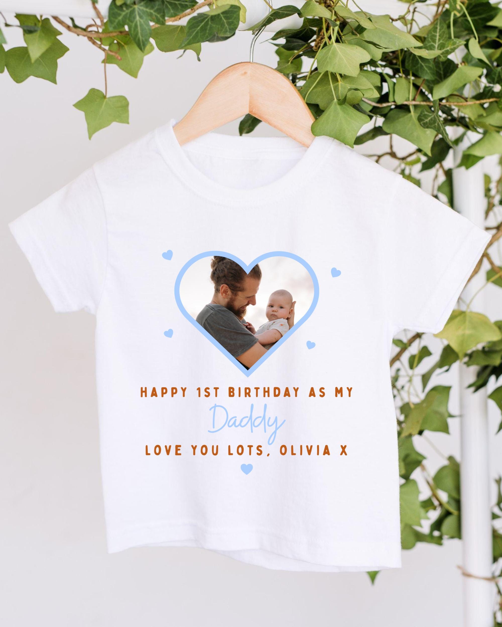 A white t-shirt with a photo of a man holding a baby inside a heart shape, along with the text "Happy 1st Birthday as my Daddy Love you lots, Olivia X".