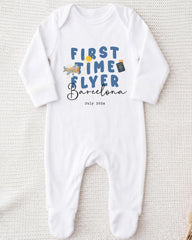 A white onesie with the text "FIRST TIME FLYER Barcelona" printed on it, along with a small airplane and a suitcase.
