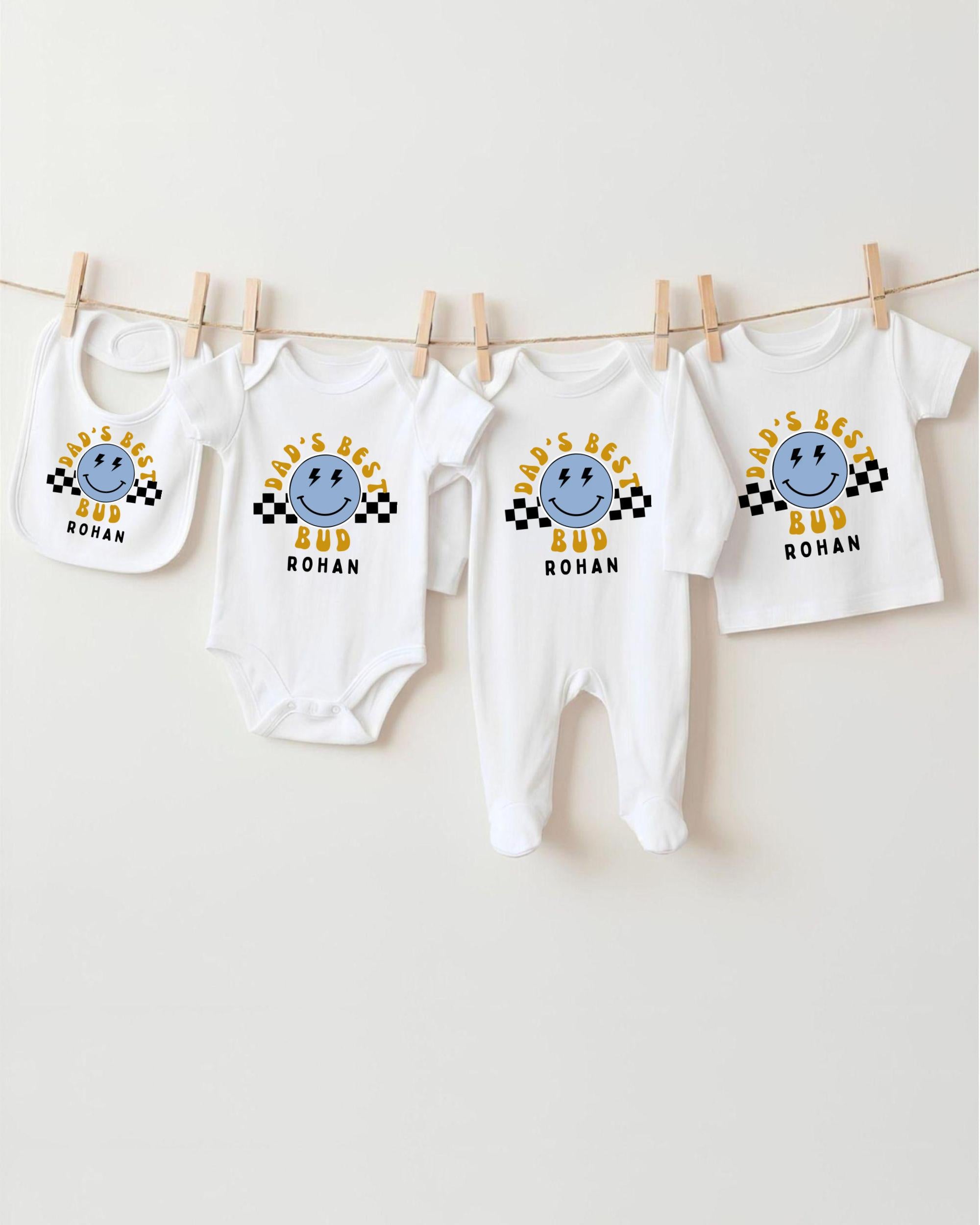 A collection of four white baby clothes, including onesies and bibs, hanging on a clothesline.