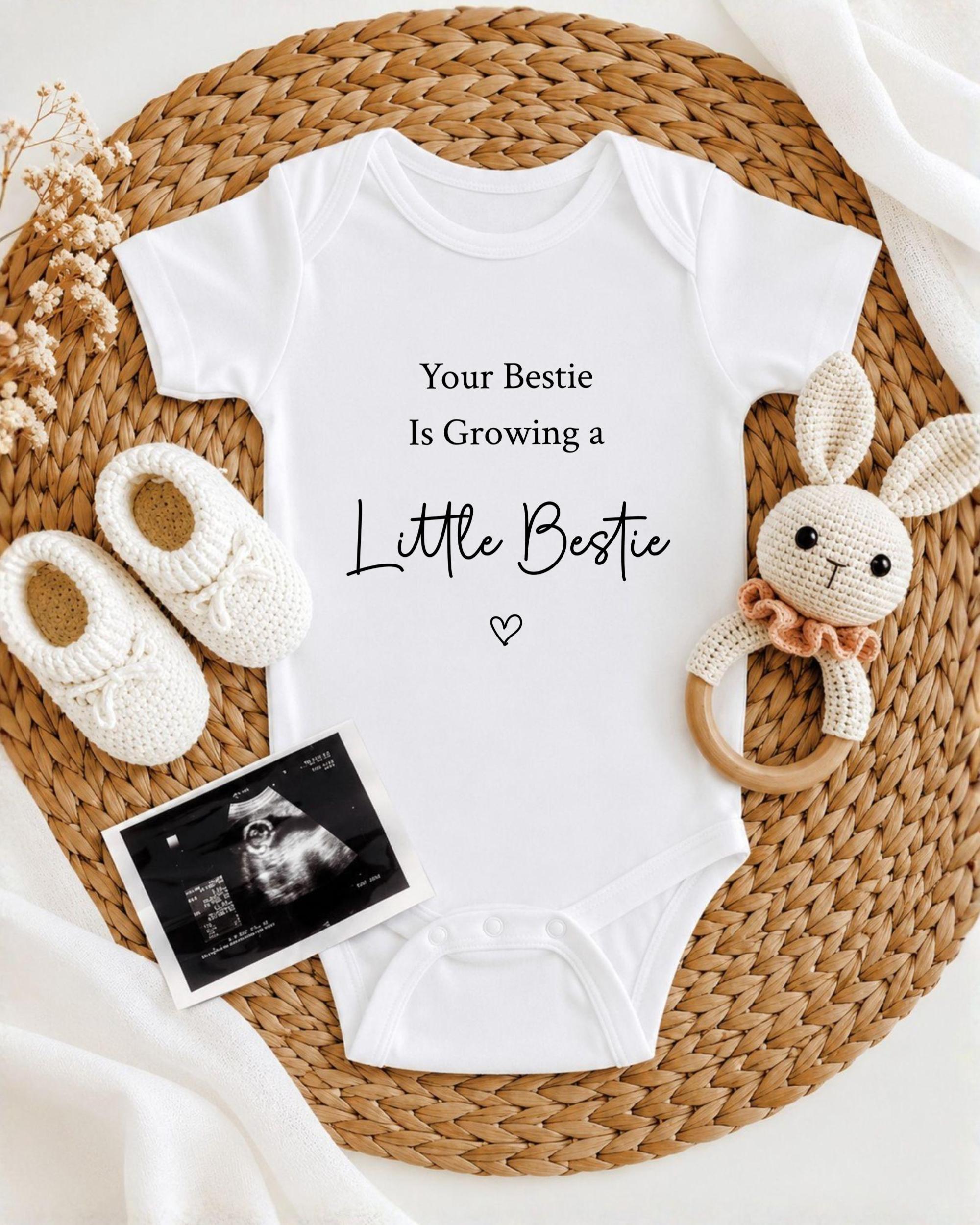 A baby onesie with the text "Your Bestie Is Growing a Little Bestie" printed on it, along with a crocheted bunny toy and a pair of white booties. There is also an image of an ultrasound scan of a baby's belly.
