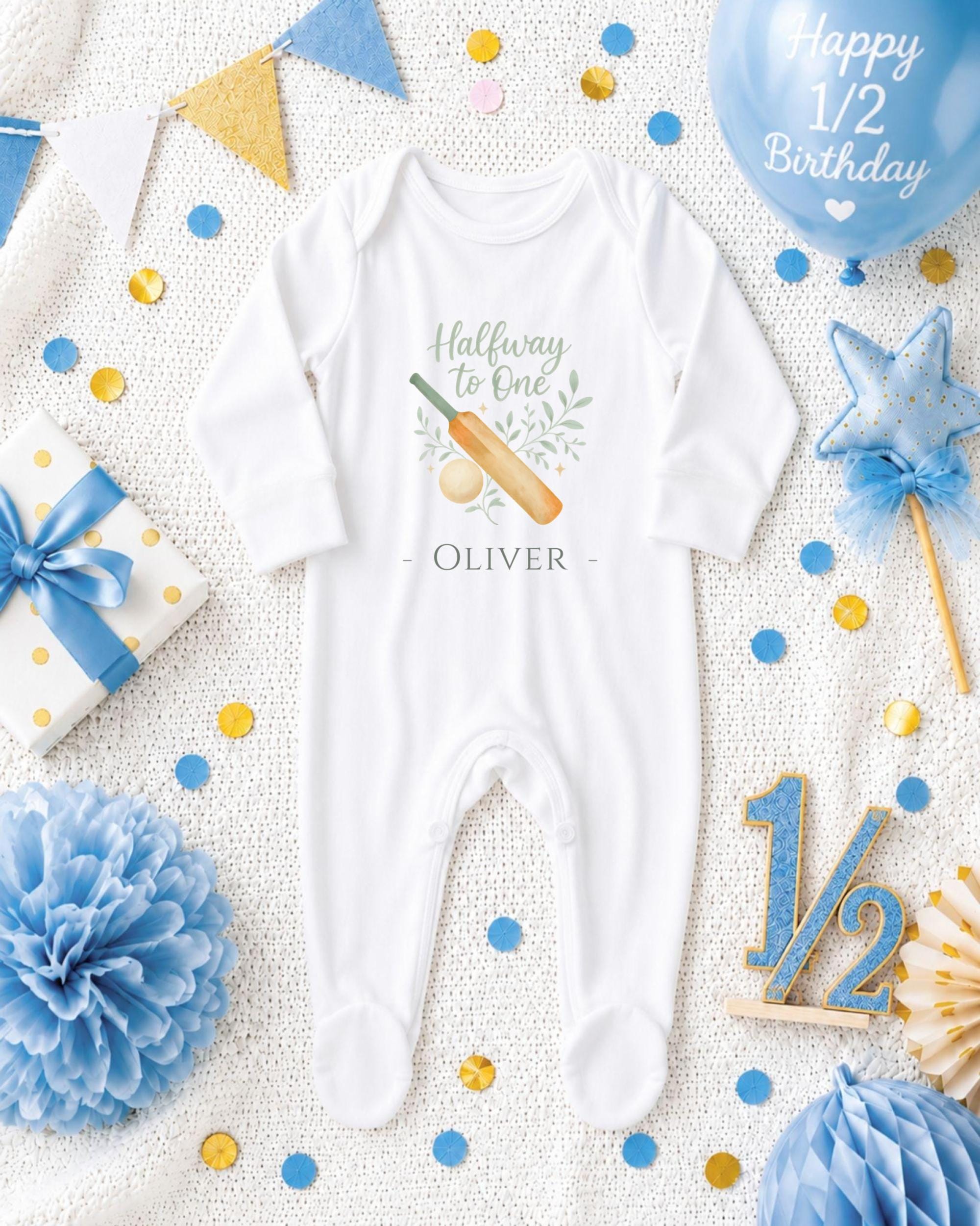 A white onesie with a cricket bat and ball design, surrounded by confetti, a blue balloon, and other baby-related items, all arranged on a white background.