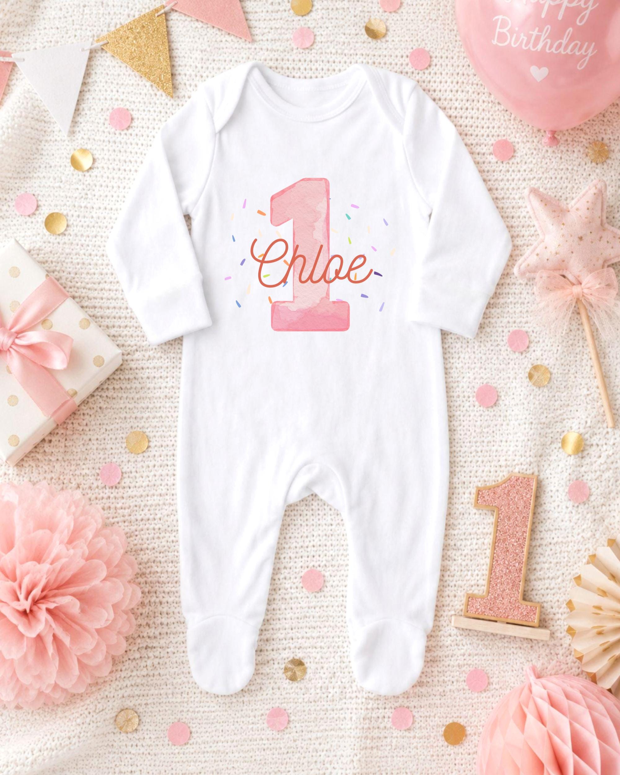 A white onesie with the name "Chloe" printed on it, surrounded by pink and gold confetti, a pink star, and other baby-themed decorations.