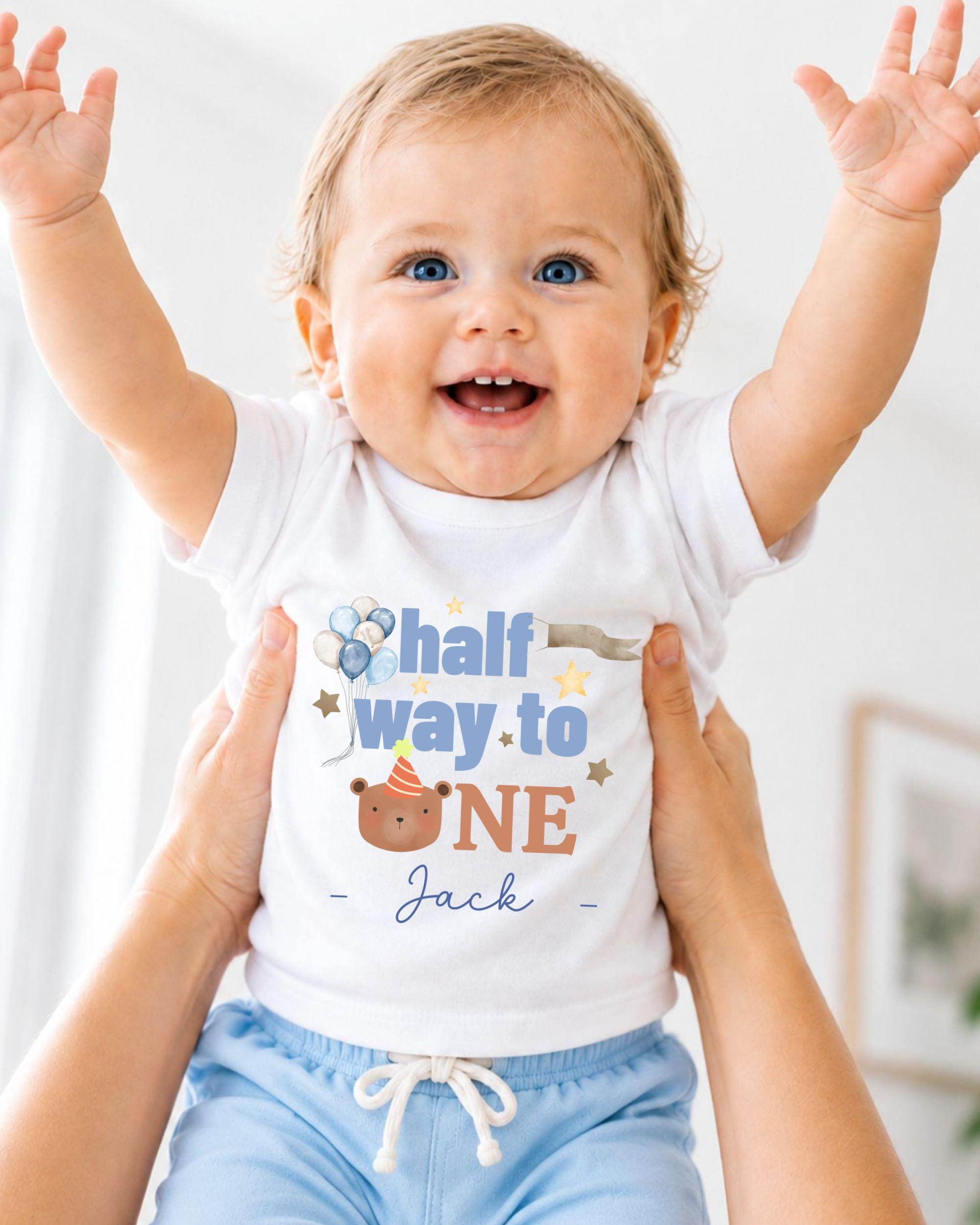 A smiling baby wearing a white onesie with a birthday message and a cartoon character.