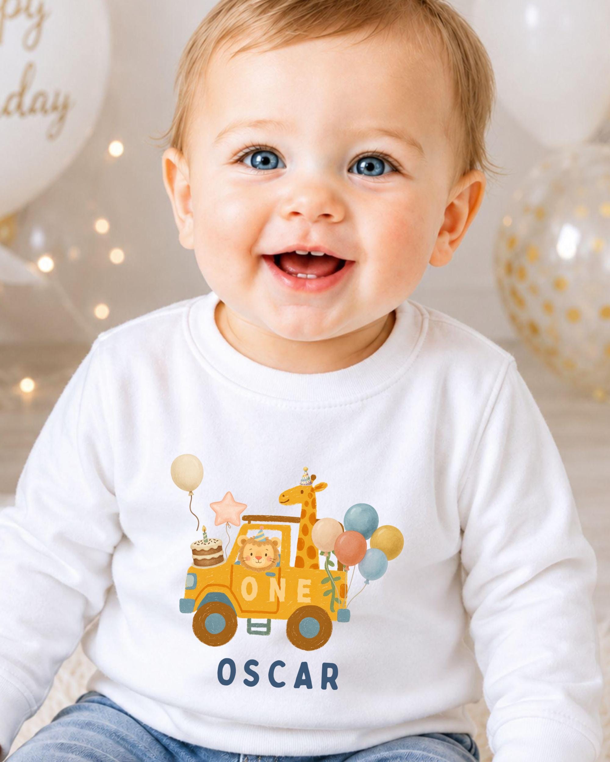 A smiling baby boy wearing a white shirt with a cartoon giraffe and a birthday truck printed on it.