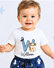 A smiling baby boy wearing a white t-shirt with a letter "W" and a ghost character, standing against a white background with blue stars.