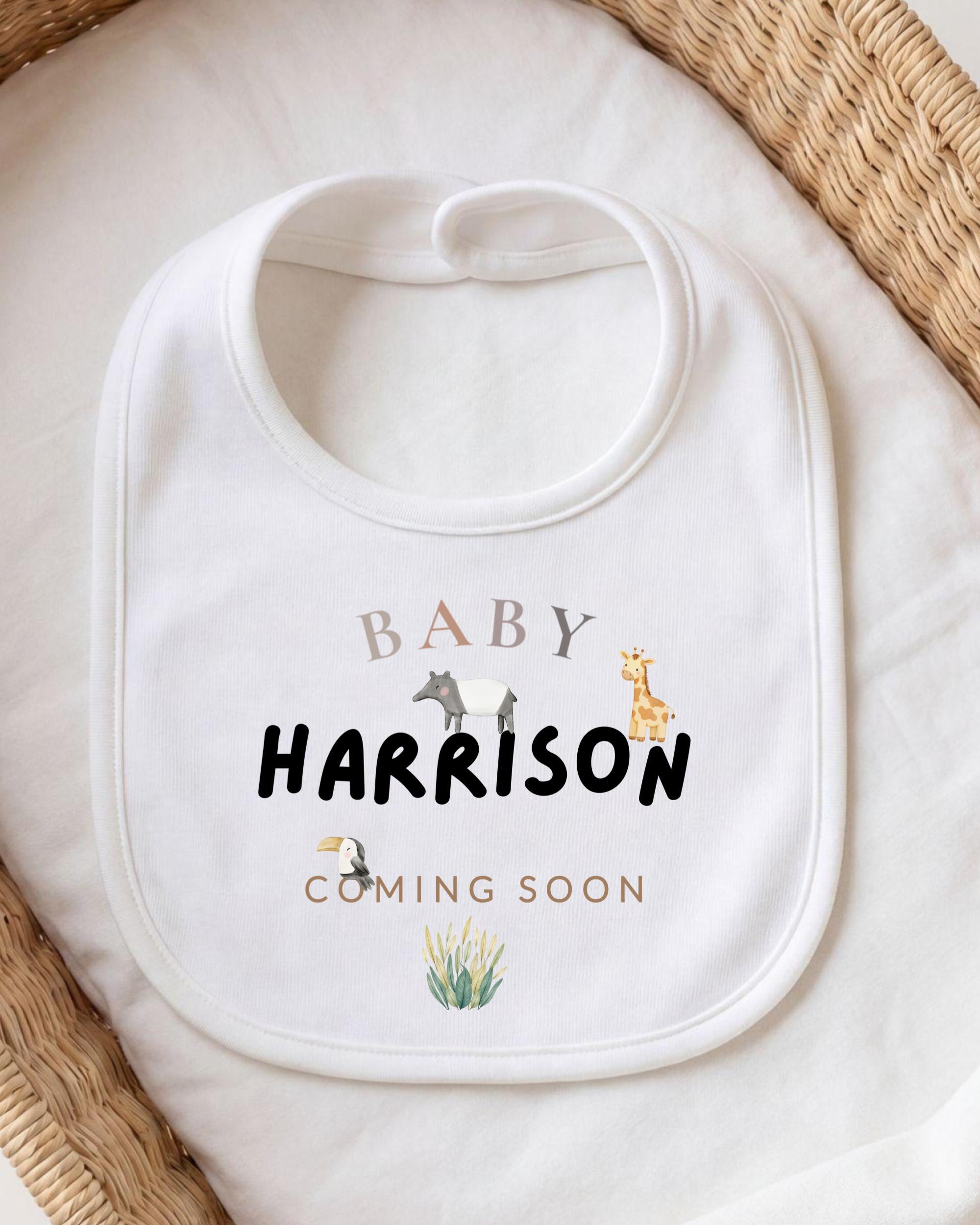 A white baby bib with the text "BABY HARRISON COMING SOON" printed on it, along with illustrations of animals.