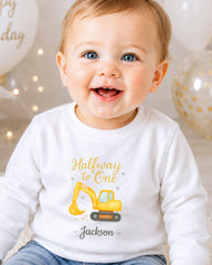 A smiling baby boy wearing a white shirt with a yellow construction vehicle graphic and the text "Halfway to One - Jackson" printed on it.