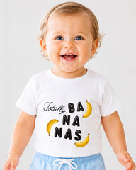A smiling baby wearing a white t-shirt with the text "Totally BANANA NAS" printed on it.
