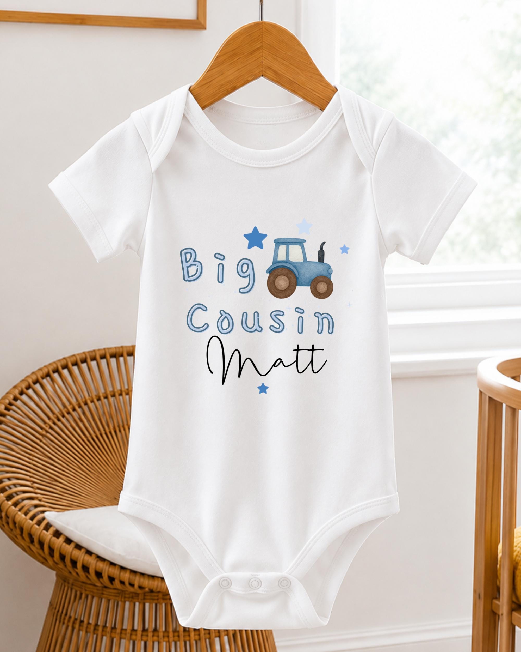 A white baby onesie with a tractor design and the text "Big Cousin Matt" printed on it.