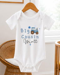 A white baby onesie with a tractor design and the text "Big Cousin Matt" printed on it.