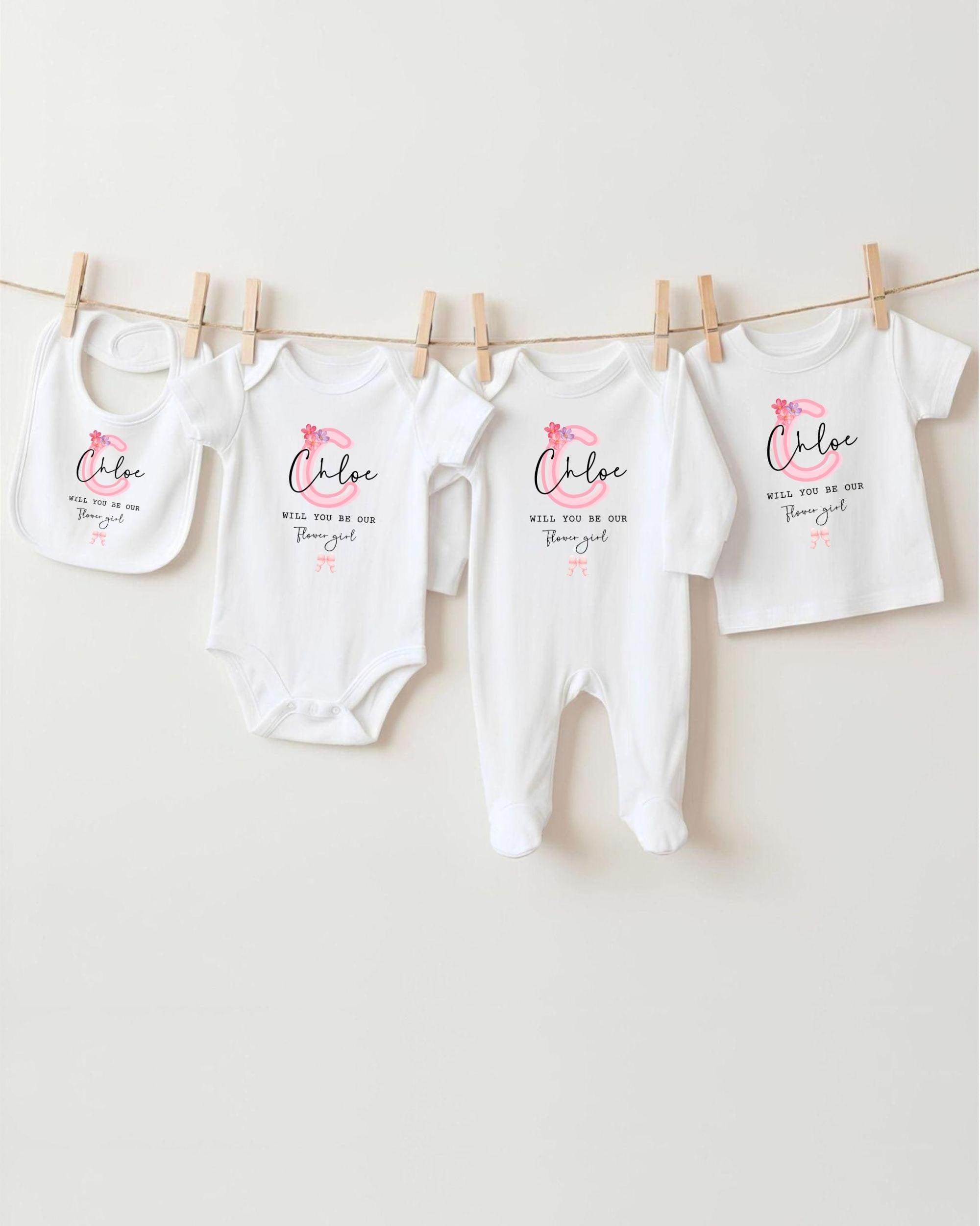 A row of four white baby clothes, including bibs and onesies, hanging on a clothesline.