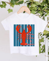 A white t-shirt with a graphic design of a red lobster on a blue striped background, hanging on a wooden hanger.