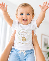 A smiling baby wearing a white t-shirt with a hedgehog graphic and the text "Halfway One" is being held up by someone's arms.