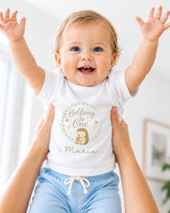 A smiling baby wearing a white t-shirt with a hedgehog graphic and the text "Halfway One" is being held up by someone's arms.