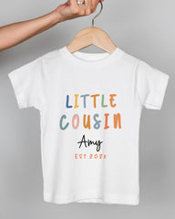 A person's hand is holding a white t-shirt with the text "LITTLE COUSIN Amy" printed on it.