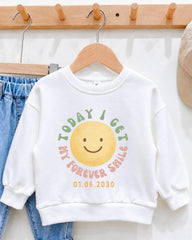 A white sweatshirt with a colorful graphic and text printed on it, hanging on a wooden hanger.