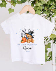 A white t-shirt with a Halloween-themed graphic design, including a teddy bear wearing a witch's hat and a spider web. The text on the t-shirt reads "My first Halloween Oscar 2023".