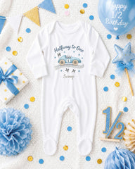 a baby onesie with a car design, surrounded by various baby-related items such as a gift, confetti, and a balloon.