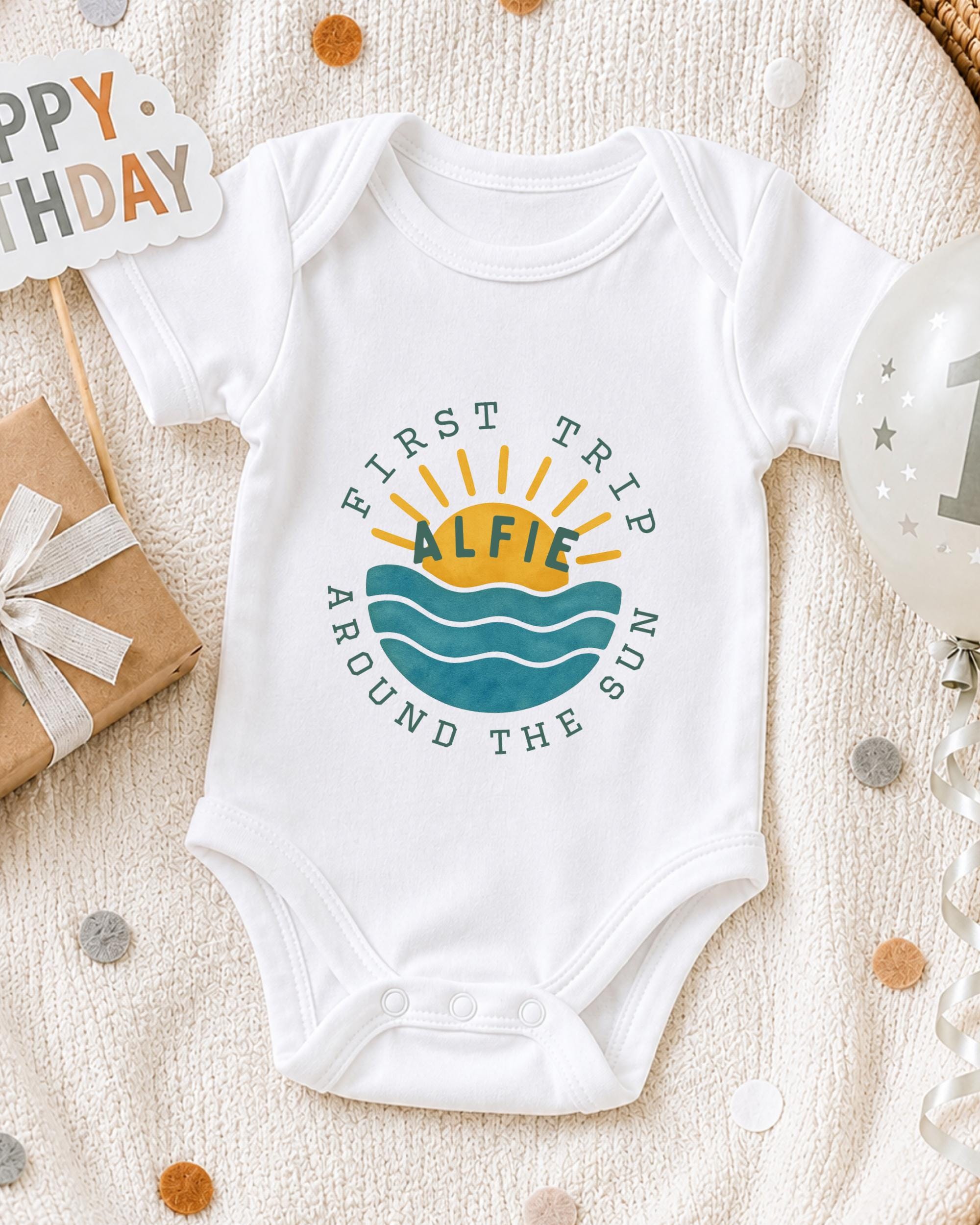 A white onesie with a graphic design on it, surrounded by a gift box, a birthday balloon, and confetti.