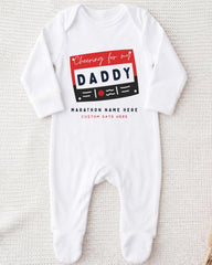 A white onesie with a graphic design on it, featuring a red and black rectangle with the text "Cheering for my DADDY" and "MARCHON NAME HERE" printed on it.