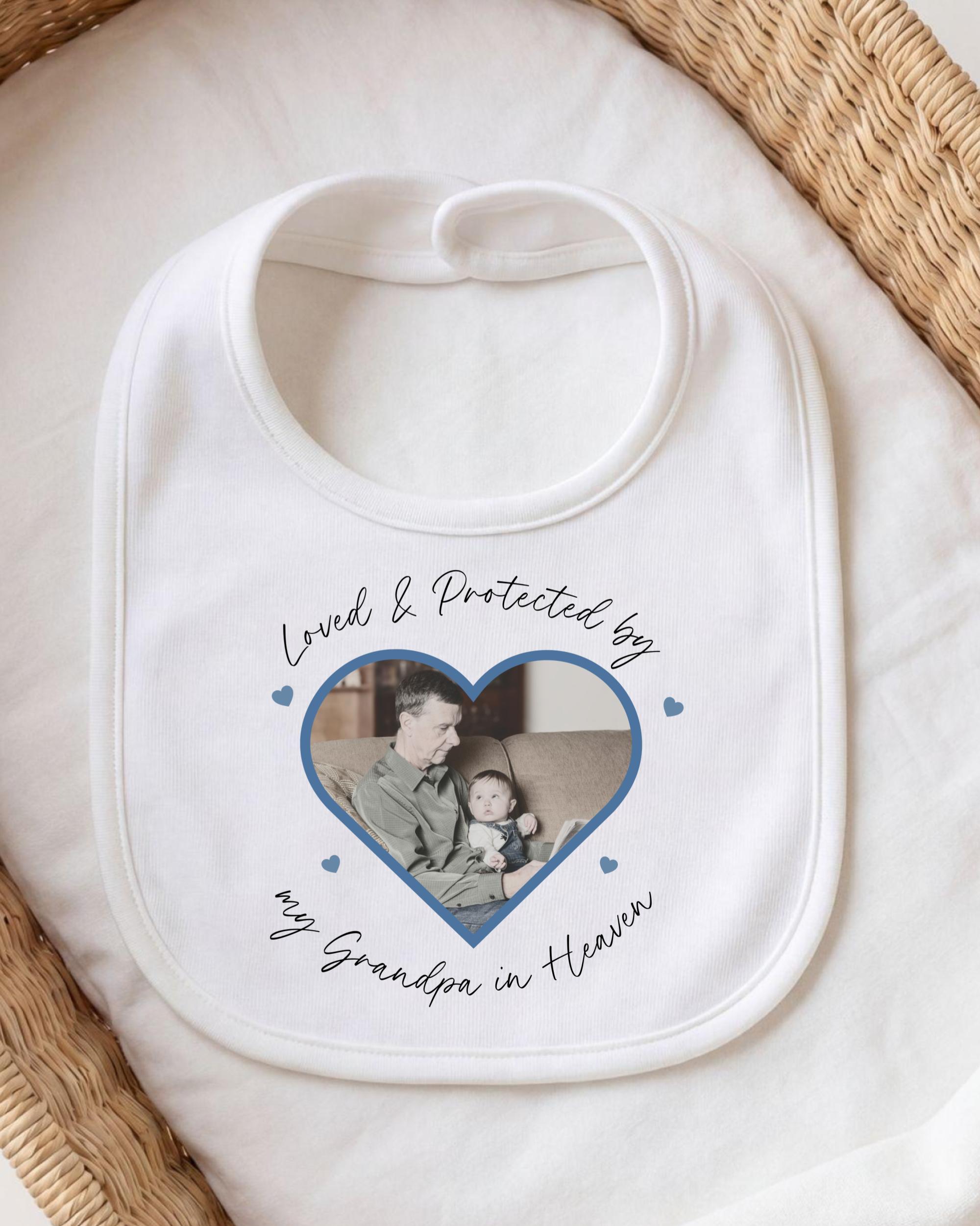 A white bib with a printed photo of a man and a child inside a heart shape, along with the text "Loved & Protected by my Grandpa in Heaven".