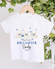 A white t-shirt with a Halloween-themed design featuring three cute ghost characters and stars. The text on the t-shirt reads "My First Halloween Emily 2020x".