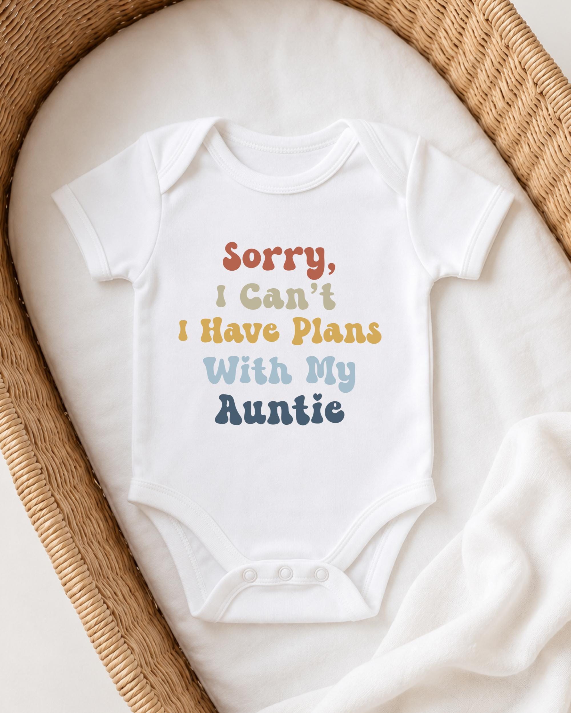 A white baby onesie with text printed on it, placed in a woven basket.